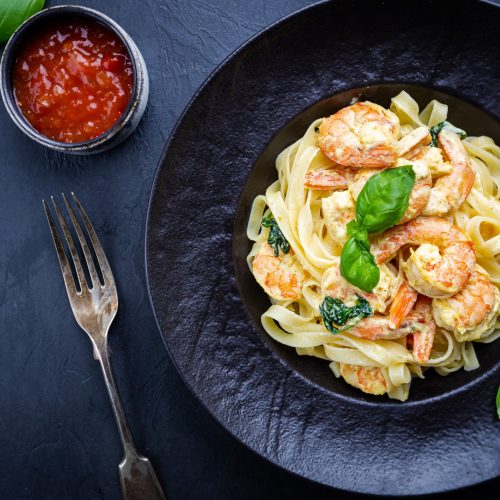 Italian pasta fettuccine in a creamy sauce with shrimp on a black plate, top view